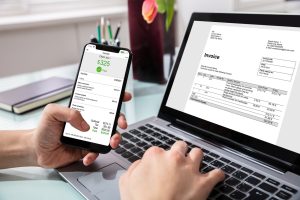 a business person is paying from phone following professional invoice on laptop screen